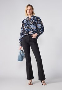 Floral blouse in dark blue with light blue and pink accents. Paired with black flared jeans and holding a light blue handbag.