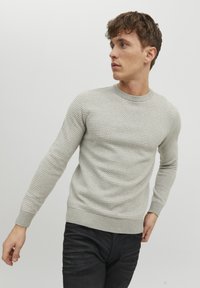 Suéter de punto gris claro con un patrón texturizado, cuello redondo y puños y dobladillo acanalados. Llevado con jeans oscuros.
