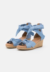 Modré látkové klínové sandály s uzlem na popruhu přes prsty a omotáním kolem kotníku. Pletená espadrilová podrážka s hladkým hnědým vnitřkem.