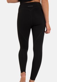 Zwarte sportleggingen gemaakt van rekbare stof met een hoge tailleband, voorzien van contourstiksels en een logo op de tailleband.