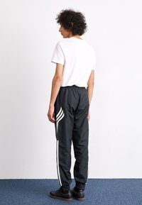 Μαύρο κολάν με λευκές ρίγες, ελαστική μέση και μανσέτες στα άκρα, σε συνδυασμό με ένα απλό λευκό T-shirt, βλέποντας από πίσω.