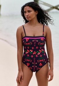 Viena gabala peldkostīms ar ziedu rakstu sarkanā un zaļā krāsā uz tumša fona, ar plānām lencītēm un strukturētu izgriezumu.