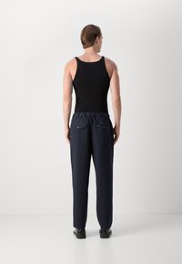 Zwarte tanktop met een aansluitend ontwerp, gecombineerd met marineblauwe broek met een elastische tailleband en twee achterzakken. Zwart schoeisel maakt de outfit compleet.