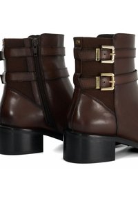 Bruine leren enkelboots met een blokhak, voorzien van zijritsen, dubbele gespdetails en elastische panelen voor extra rek. Gladde afwerking.