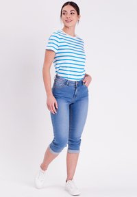 Conjunto de mujer que incluye una camiseta de rayas blancas y azules y unos vaqueros cortos de color azul claro con puños doblados, combinados con zapatillas blancas.