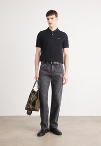 Navy polo shirt with three buttons, dark gray straight-leg jeans, black shoes, and an olive green bag with brown accents. Smooth textures.