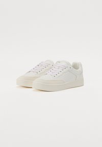 White sneakers featuring a smooth leather upper, rounded toe, and a flat rubber sole. Includes subtle perforations and matching laces.