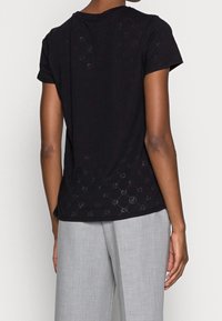 Sort T-shirt med korte ærmer, der har et subtilt mønster, blød tekstur og afslappet pasform. Kombineret med lysegrå bukser med bred ben.