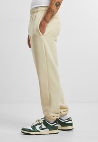 Beige sweatpants med elastisk talje og sidelommer. Materialet ser blødt ud; har en afslappet pasform med tapered manchetter.