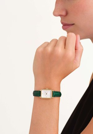 Reloj con correa de cuero de cocodrilo verde, con una esfera blanca cuadrada y acentos dorados, que exhibe un diseño minimalista y una textura sutil.