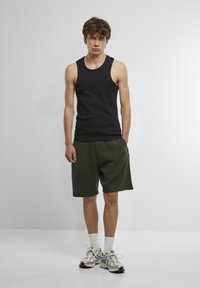 Schwarzes ärmelloses Tanktop kombiniert mit grünen gemusterten Shorts, weißen Socken und silbernen Sportschuhen. Einfaches Design, lässige Passform.
