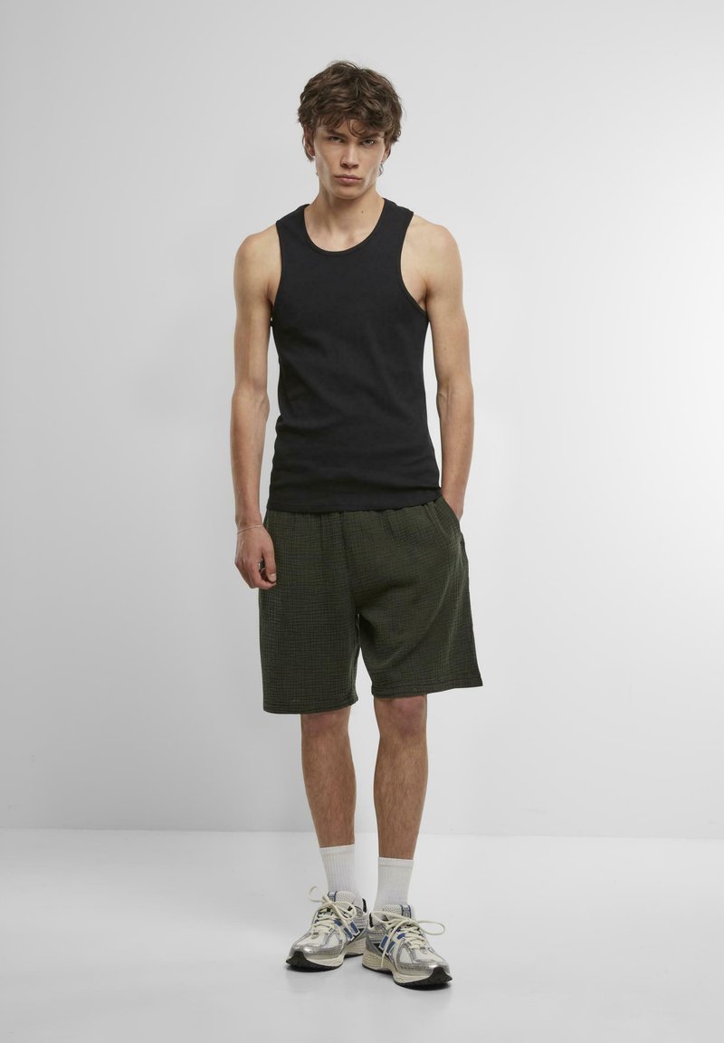 Zwarte mouwloze tanktop gecombineerd met groene kortebroek met patroon, witte sokken en zilveren sportschoenen. Eenvoudig ontwerp, casual pasvorm.