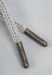 Cuerdas de zapato trenzadas de color gris con extremos metálicos, que presentan texto grabado en una superficie texturizada, unidas en ambos extremos.