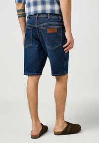 Jeans kratke hlače v temno modri barvi s klasičnim dizajnom, ki vključujejo rjav usnjen pečat na hrbtu in dvojno šivane žepe.