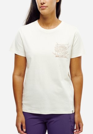 Woman wearing a white short-sleeve t-shirt with a floral line art design on the left chest and purple pants against a white background.