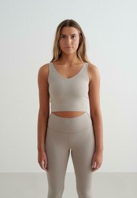 Beezhivärvi sportlik crop top V-kaelusega ja lõikega, koos kõrge vöökohaga retuusidega sobivas kangas ja värvitoonis.