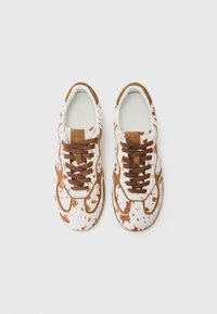 Sneakers with a white base featuring a brown splatter pattern. Brown suede accents around the eyelets and tongue. Brown laces.