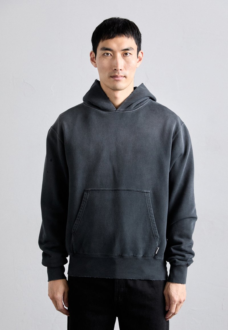 Sudadera de color gris oscuro con un bolsillo frontal, ajuste holgado y capucha con cordón. Fabricada en un tejido suave y texturizado con detalles de dobladillo deshilachado.