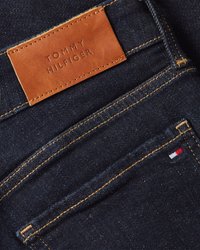 Ciemnoniebieskie dżinsy z brązową skórzaną łatą z napisem "TOMMY HILFIGER". Posiadają pomarańczowe przeszycia oraz małą haftowaną flagę w kolorach czerwonym, białym i niebieskim.