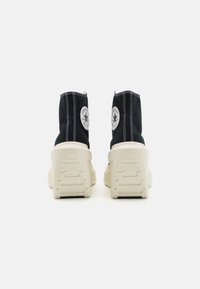 Zwarte canvas enkelboots met een gewatteerde witte zool, voorzien van witte stiksels en een circulair logo op de achterkant.