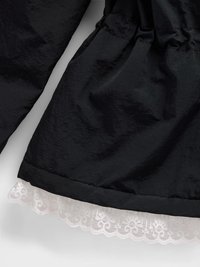 Sort jakke med struktureret overflade, der har en samlet talje og en hvid blondekant i kanten.