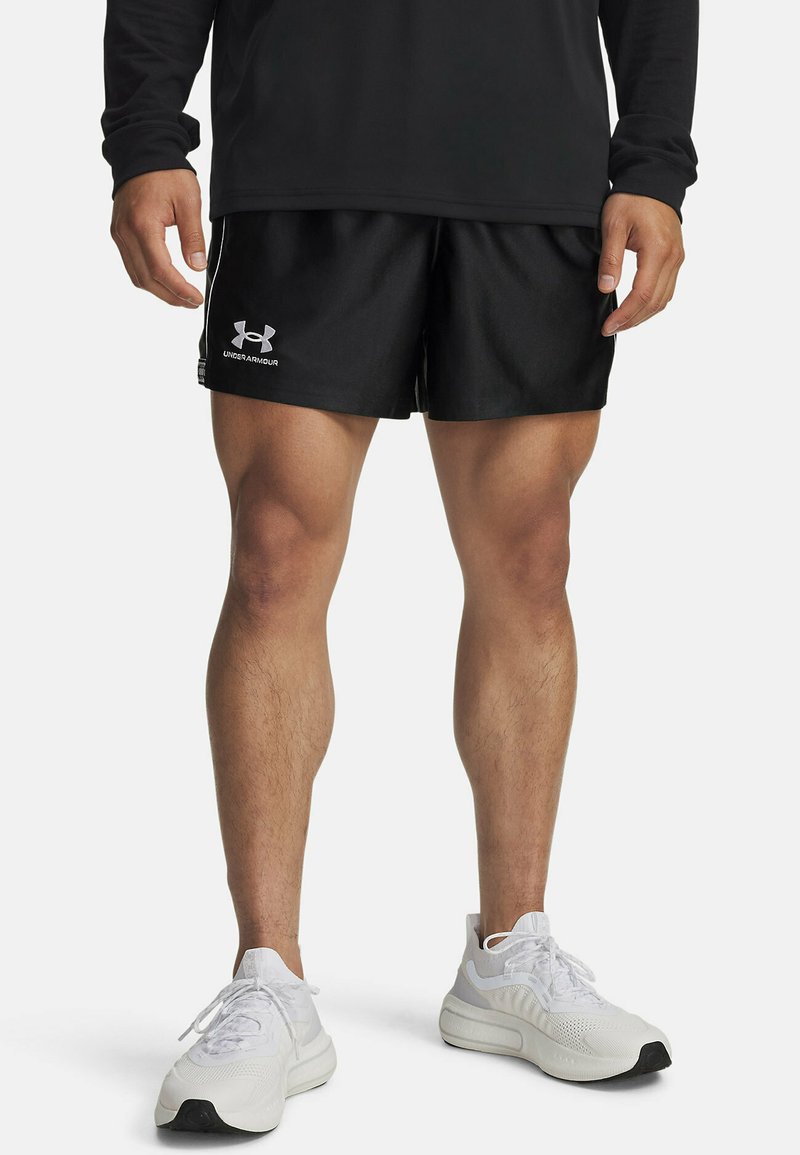 Črne športne hlače z belim logotipom Under Armour, v kombinaciji z belimi supergami. Gladek material, elastičen pas in podrobnosti stranskih črt.