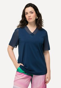 Námořnická modrá blůza s výstřihem do V, krátkými průsvitnými rukávy a uvolněným střihem, doplněná o kalhoty s růžovými a zelenými vzory.