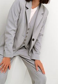 Costume gris ajusté avec un revers cranté, fermeture à un bouton et gilet ajusté, présentant une texture raffinée et un motif à rayures discrètes.