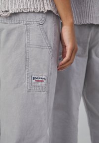 Svetlo sivi BDG džins značajnu imaju cargo džep s logom, detalje šivanja i opušteni kroj. Materijal izgleda mekano i izdržljivo.