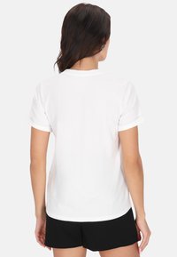 Vit kortärmad t-shirt med uppvikta ärmar och rundad halsringning, med en slät yta och avslappnad passform. Visad bakifrån.