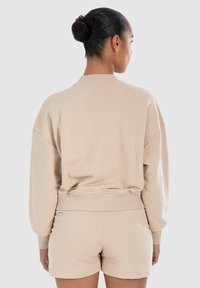 Sweatshirt beige avec un col rond et un ourlet côtelé, présentant des épaules tombantes et une coupe décontractée, associé à un short assorti.