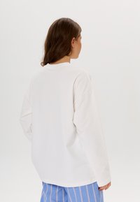 Witte blouse met lange mouwen en een ontspannen pasvorm, ronde halslijn en ingezette schouders, gecombineerd met lichtgewicht blauwe gestreepte broek.
