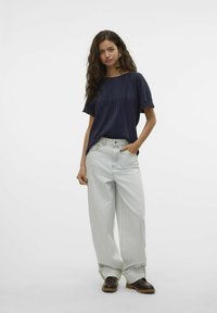 Marineblå plisseret kortærmet top, parret med lyse denim bredbenede bukser og brune platform sko. Enkel, afslappet design.