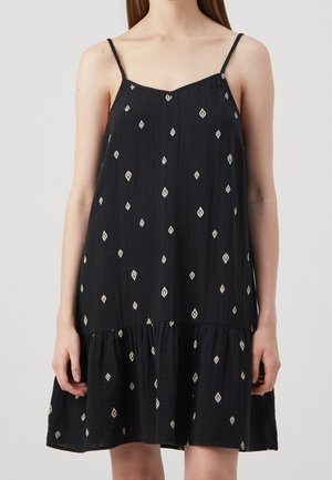 Vestido negro sin mangas con un corte relajado, que presenta patrones en forma de diamante blancos y un dobladillo en capas, hecho de una tela ligera.
