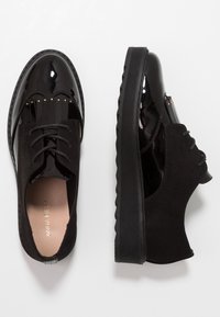 Chaussures noires avec un avant en vernis brillant et des côtés en daim mat. Elles présentent un design à lacets, des plis décoratifs et une semelle texturée épaisse.