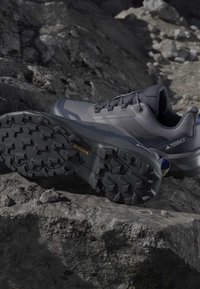Γκρι και μαύρα παπούτσια πεζοπορίας Adidas Terrex σε πετρώδες έδαφος, με επιθετικά λάστιχα Continental για καλύτερη πρόσφυση σε εξωτερικούς χώρους.