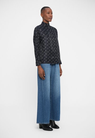 Zwart gedessineerde langdurige mouwen blouse met een hoge kraag, gecombineerd met wijdlopende lichtblauwe spijkerbroek en zwarte haklaarzen.
