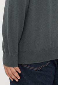 Sweater en maille gris foncé avec un col rond et des poignets côtelés, associé à un jean en denim foncé avec des détails de couture jaune.