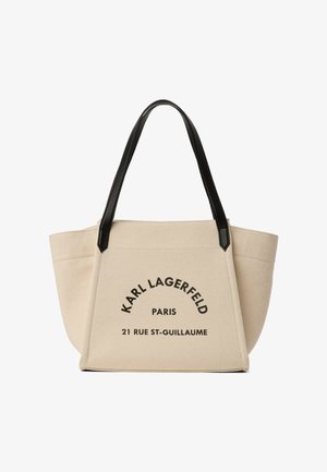 Beżowa torba na ramię z płótna z czarnymi uchwytami, z napisem "KARL LAGERFELD PARIS 21 RUE ST-GUILLAUME" nadrukowanym na czarno z przodu.