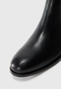 Botín de cuero negro hasta el tobillo con puntera puntiaguda, textura suave y silueta elegante. Suela baja y plana para mayor estabilidad.