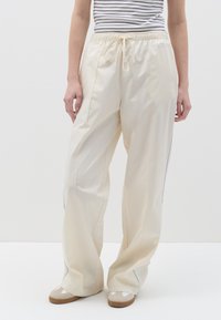 Pantalones de color crema claro con cintura elástica y cordón. Presentan un ribete azul a lo largo de las costuras laterales. Diseño de corte holgado.