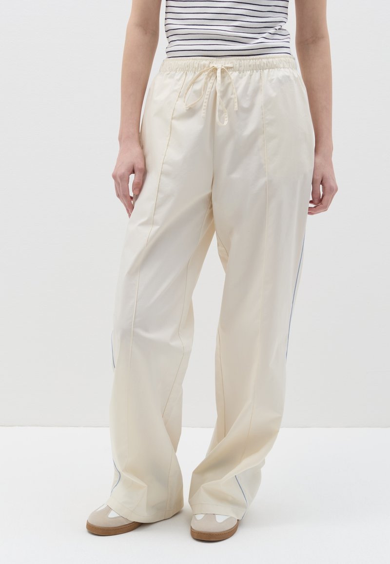 Pantalones de color crema claro con cintura elástica y cordón. Presentan un ribete azul a lo largo de las costuras laterales. Diseño de corte holgado.
