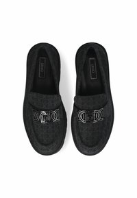 Schwarze Loafers mit einem gemusterten Obermaterial, silbernem Logo-Detail und einer dicken, strukturierten Sohle für zusätzlichen Grip. Die gedrehte Ansicht zeigt das Innenetikett.