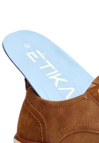 Zapato de ante marrón con plantilla azul marcadas con "42" y "ËTIKA" en letras blancas. Presenta una puntera redondeada y un detalle de costura en contraste.