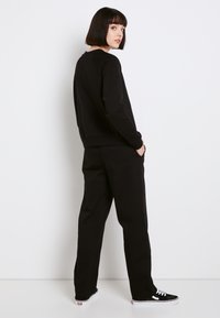 Sudadera negra de manga larga, con puños acanalados y cuello redondo, combinada con pantalones negros a juego y zapatillas negras con detalles en blanco.