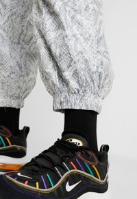 Svarta sneakers med flerfärgade accenter, med en böjd sula och Nike-logotyp. Grå byxor med ormskinnsmönster och elastiskt avslut syns också.