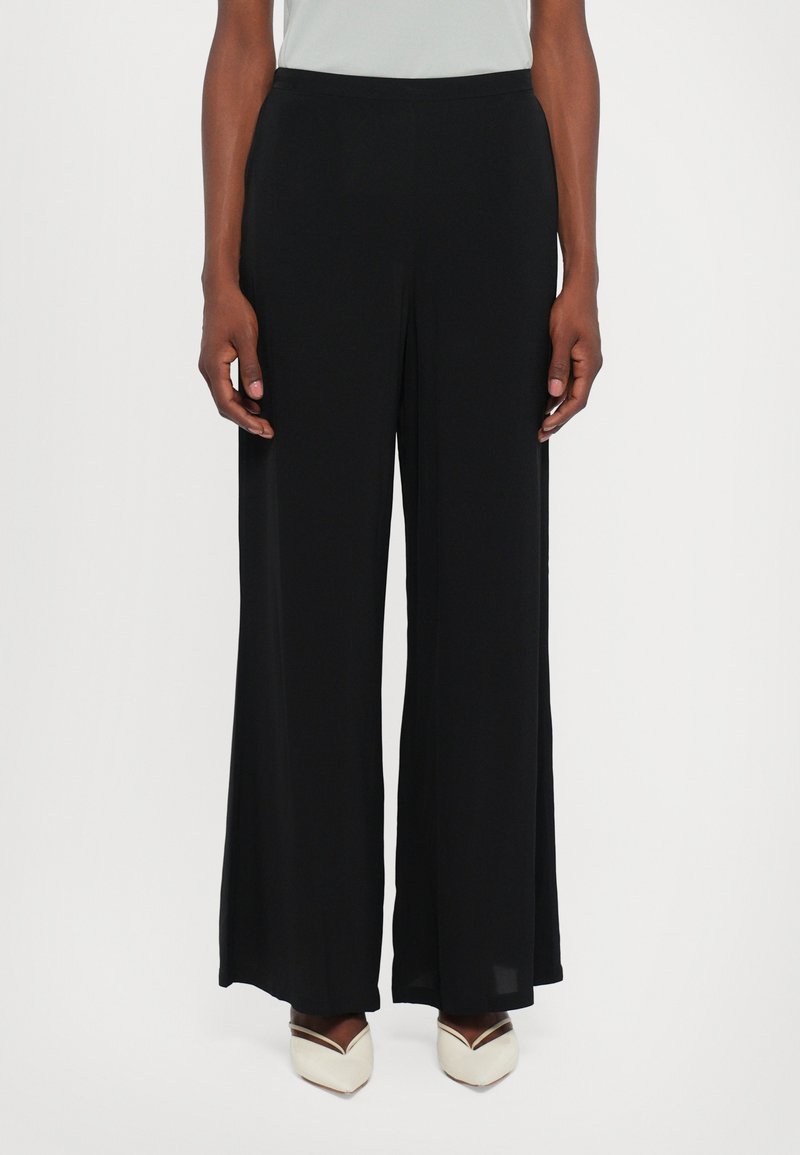 Pantaloni neri a gamba larga realizzati in un tessuto leggero e liscio. Presentano una vita alta con un elastico e una silhouette fluida.