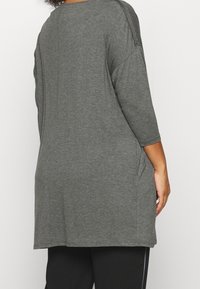 Tunique grise à manches trois-quarts, en tissu doux. Comprend des poches latérales et une coupe ample, avec un ourlet arrondi.