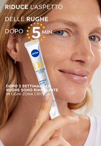 Siero antirughe NIVEA Q10 in un tubo bianco con dettagli blu e gialli. Texture liscia, tenuto tra le dita, su uno sfondo chiaro.