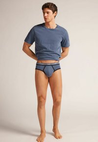 Męska niebieska koszulka bawełniana w połączeniu z ciemnoniebieskimi slipami. Miękka tkanina, okrągły dekolt, krótki rękaw i minimalistyczny design z kontrastowymi akcentami.